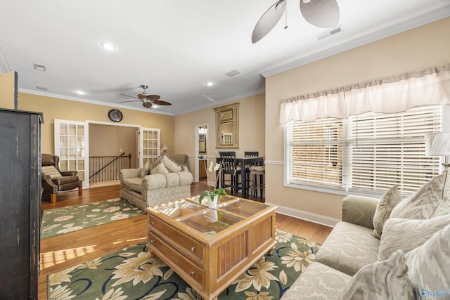 living area with wood finished floors, a ceiling fan, baseboards, visible vents, and crown molding