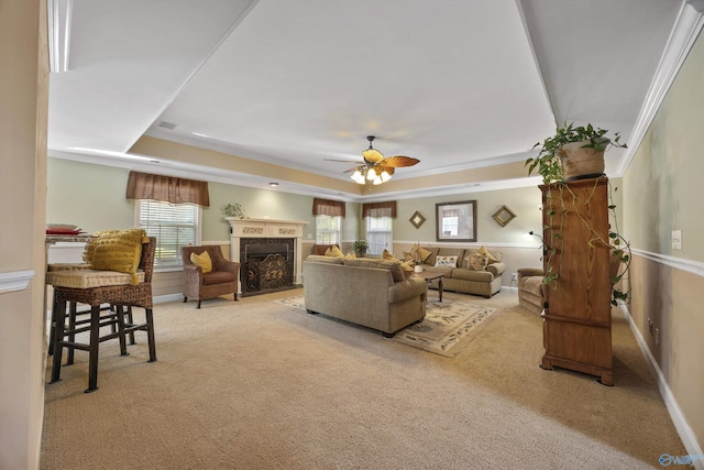 carpeted living area featuring ceiling fan, a fireplace, ornamental molding, and a raised ceiling