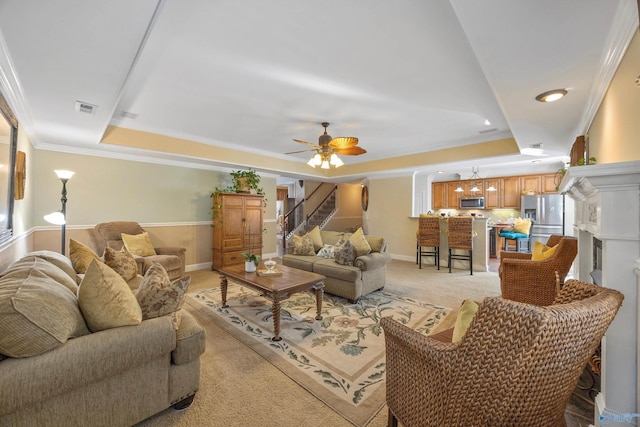 living area featuring visible vents, light colored carpet, stairway, ornamental molding, and a tray ceiling