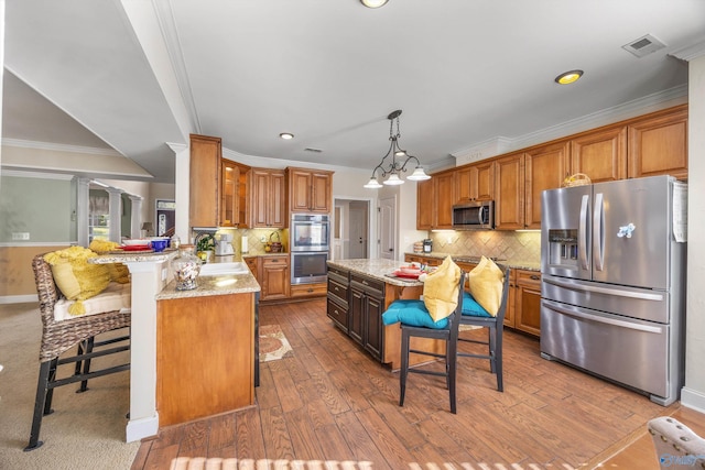 kitchen featuring hardwood / wood-style floors, light stone countertops, stainless steel appliances, kitchen peninsula, and a breakfast bar