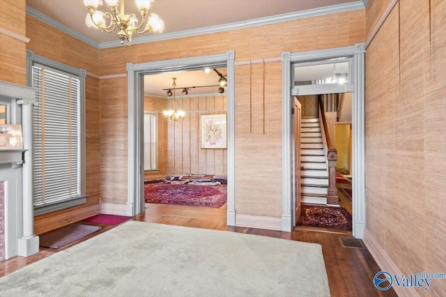 doorway to outside featuring wooden walls, a chandelier, dark hardwood / wood-style floors, and ornamental molding