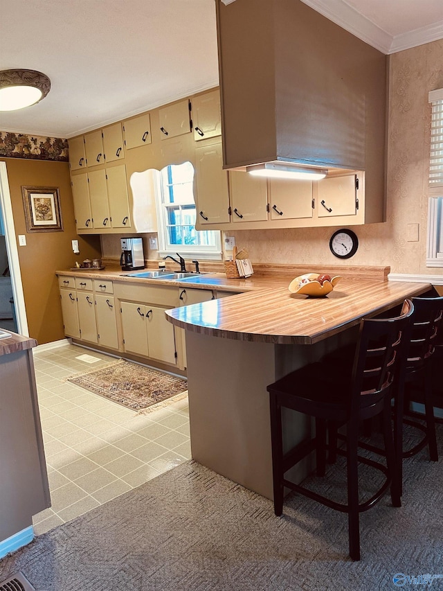 kitchen featuring kitchen peninsula, a breakfast bar, crown molding, sink, and cream cabinetry