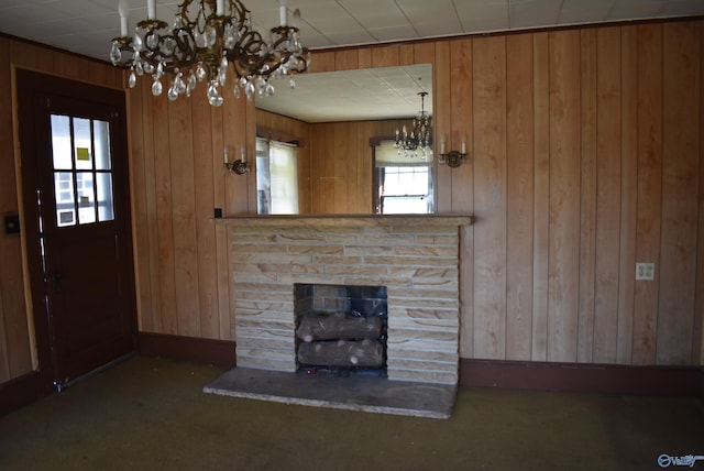 unfurnished living room featuring a fireplace, dark colored carpet, wooden walls, and a notable chandelier