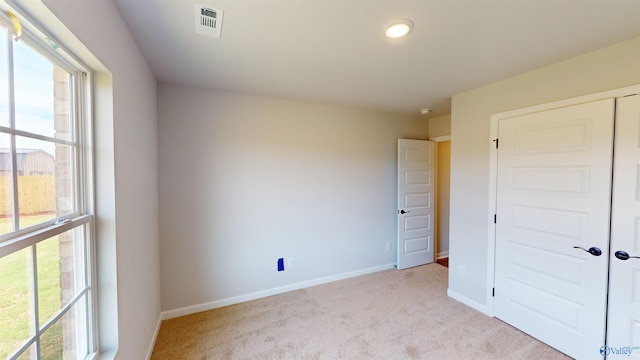 unfurnished bedroom with multiple windows, light carpet, and a closet