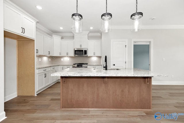 kitchen featuring stainless steel appliances, white cabinetry, a kitchen island with sink, and decorative light fixtures