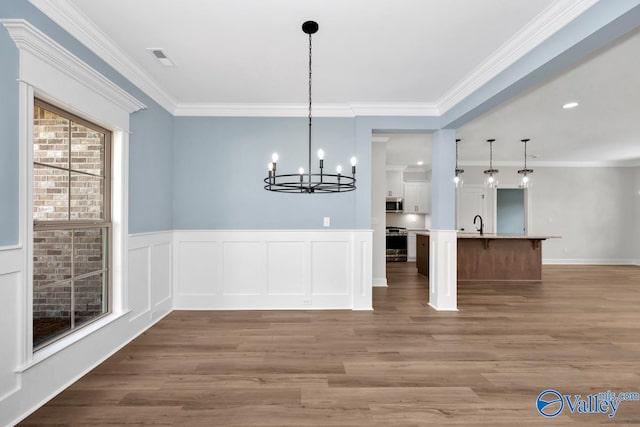 unfurnished dining area featuring an inviting chandelier, sink, hardwood / wood-style floors, and crown molding