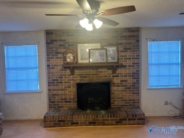 unfurnished living room featuring ceiling fan, a textured ceiling, a brick fireplace, and a healthy amount of sunlight