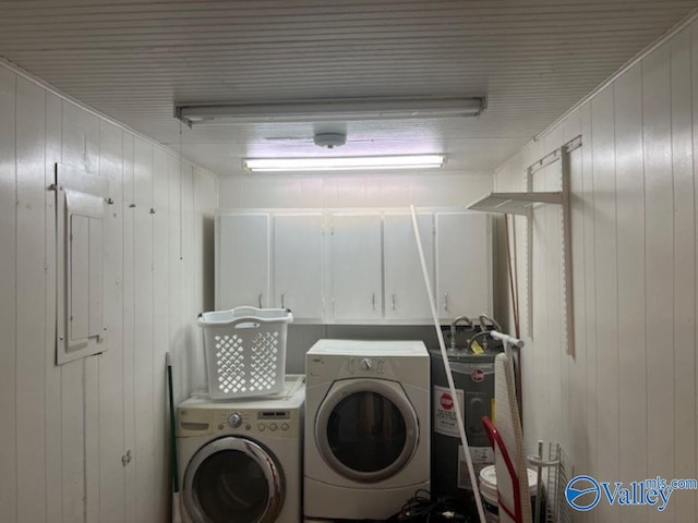 laundry room with cabinets, water heater, wood walls, and washer and dryer