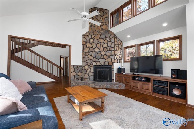 living room with ceiling fan, a stone fireplace, dark hardwood / wood-style flooring, and high vaulted ceiling