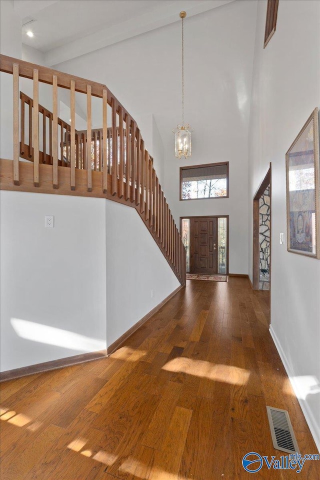 foyer entrance featuring wood-type flooring, a towering ceiling, and an inviting chandelier