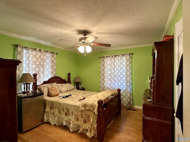 bedroom with ceiling fan, ornamental molding, a textured ceiling, multiple windows, and light hardwood / wood-style floors