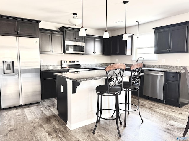 kitchen with stone countertops, a center island, hanging light fixtures, stainless steel appliances, and hardwood / wood-style floors