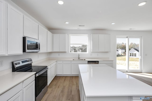 kitchen featuring a kitchen island, appliances with stainless steel finishes, white cabinetry, sink, and light hardwood / wood-style floors