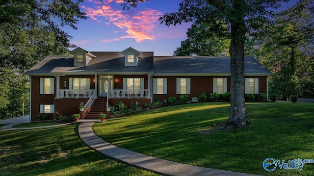 cape cod home with covered porch and a lawn