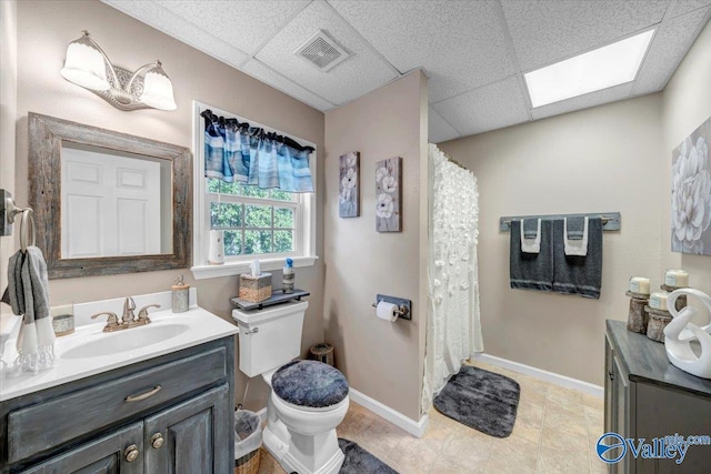 bathroom featuring vanity, a skylight, toilet, and a drop ceiling