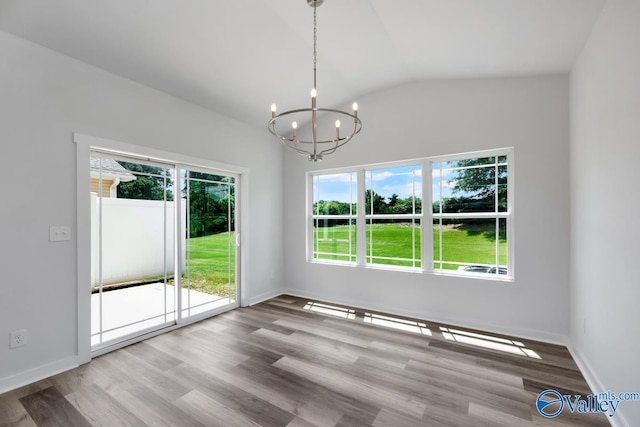 empty room with a notable chandelier, vaulted ceiling, baseboards, and wood finished floors