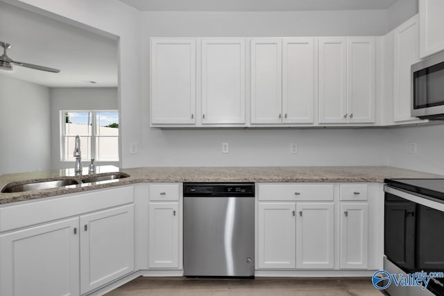 kitchen with appliances with stainless steel finishes, a sink, light stone counters, and white cabinets