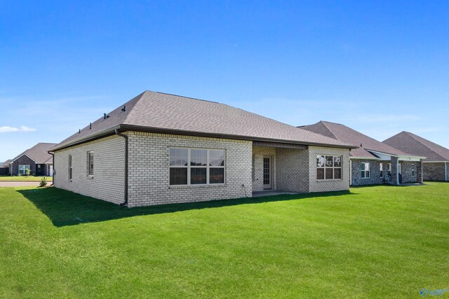 rear view of property with roof with shingles, brick siding, and a lawn