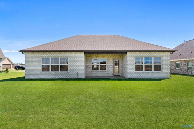 rear view of property featuring roof with shingles, a lawn, and brick siding