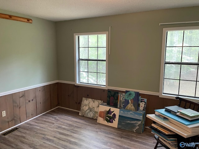unfurnished room featuring a wainscoted wall, wood finished floors, visible vents, and a textured ceiling