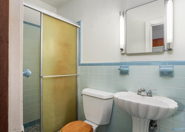 bathroom featuring toilet, a shower stall, tile walls, wainscoting, and a sink