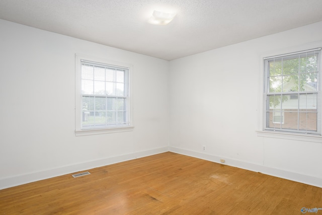 unfurnished room with light wood-type flooring, plenty of natural light, baseboards, and a textured ceiling