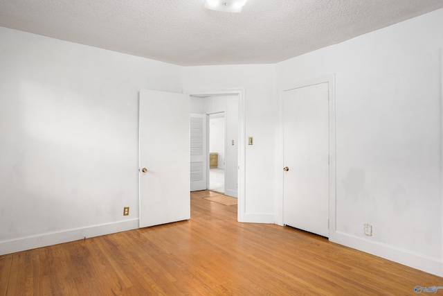 unfurnished room with light wood finished floors, baseboards, and a textured ceiling