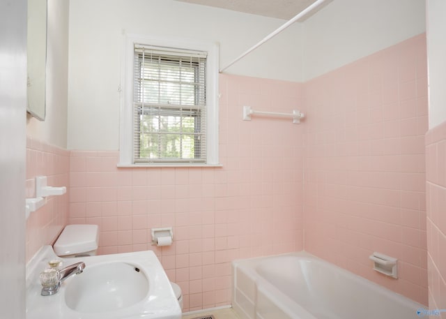 bathroom with a sink, toilet, tile walls, and  shower combination