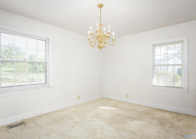 carpeted spare room featuring plenty of natural light, a chandelier, and baseboards