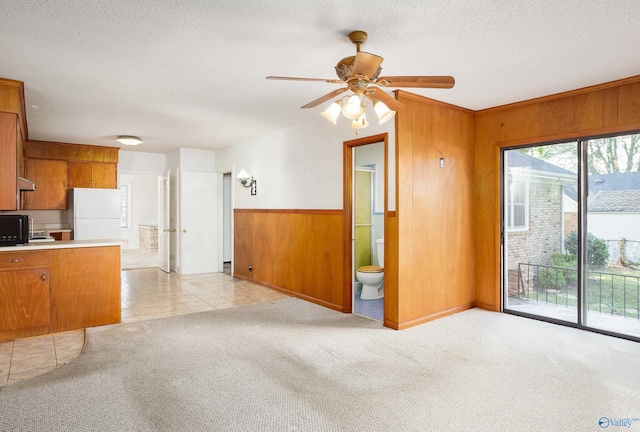 kitchen featuring freestanding refrigerator, wood walls, brown cabinetry, light colored carpet, and ceiling fan