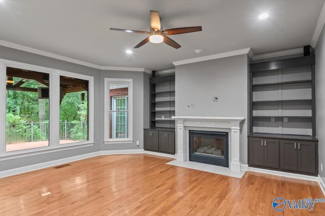 unfurnished living room featuring a premium fireplace, crown molding, a wealth of natural light, and light hardwood / wood-style floors