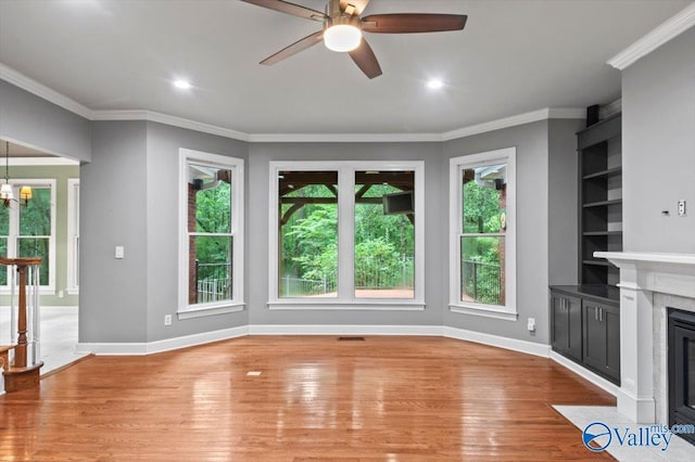 unfurnished living room featuring ceiling fan with notable chandelier, built in features, ornamental molding, light hardwood / wood-style floors, and a premium fireplace