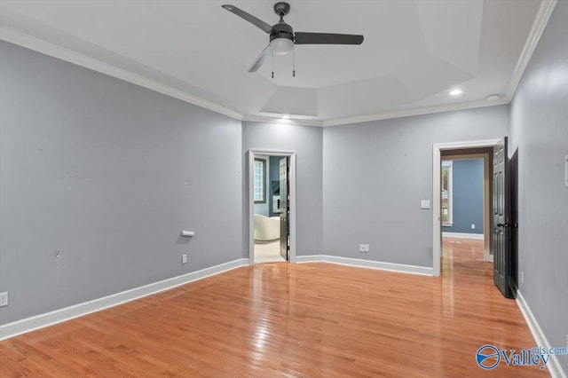 empty room with a raised ceiling, crown molding, ceiling fan, and light hardwood / wood-style flooring