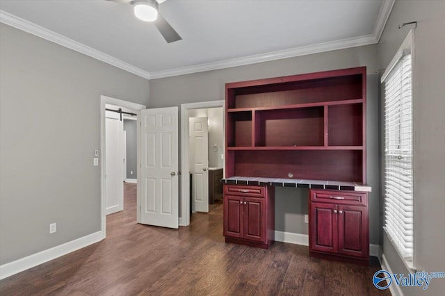 unfurnished office featuring crown molding, ceiling fan, dark hardwood / wood-style floors, built in desk, and a barn door