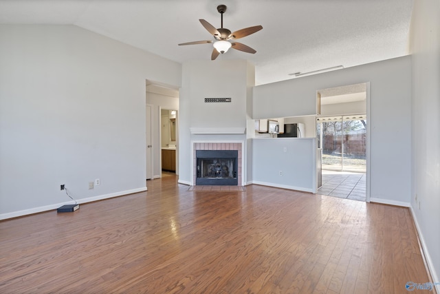 unfurnished living room with ceiling fan, wood-type flooring, a tiled fireplace, and lofted ceiling