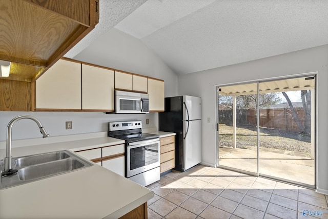 kitchen with appliances with stainless steel finishes, lofted ceiling, sink, light tile patterned floors, and a textured ceiling