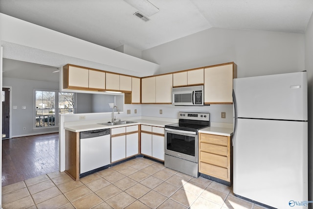 kitchen with lofted ceiling, sink, light tile patterned floors, stainless steel appliances, and kitchen peninsula