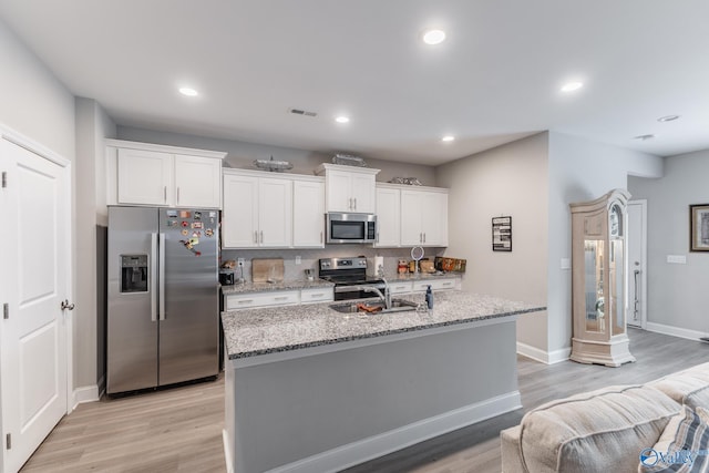 kitchen featuring stainless steel appliances, light wood-style flooring, a center island with sink, and white cabinetry