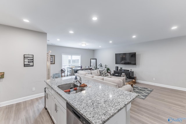 kitchen with a kitchen island with sink, white cabinets, a sink, and light wood finished floors