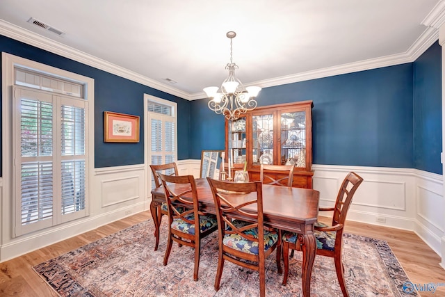 dining space with light wood finished floors, a chandelier, crown molding, a wainscoted wall, and visible vents