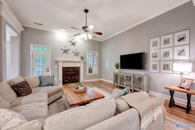 living room featuring crown molding, ceiling fan, a high end fireplace, baseboards, and light wood-type flooring
