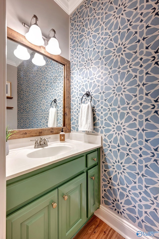 bathroom with ornamental molding, wallpapered walls, wood finished floors, and vanity