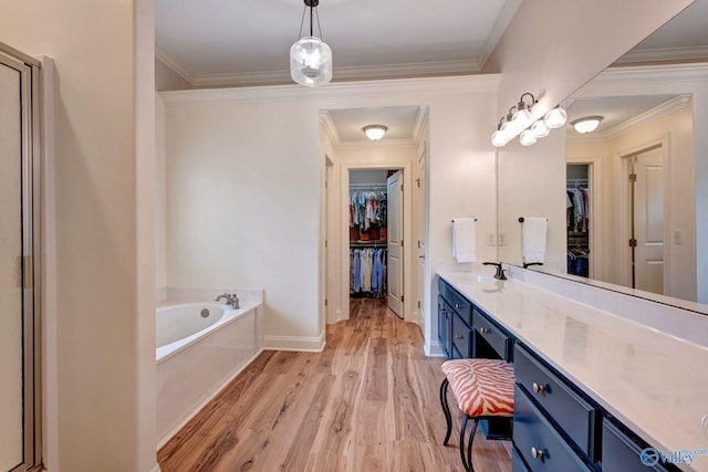 full bathroom featuring vanity, ornamental molding, a walk in closet, a garden tub, and wood finished floors