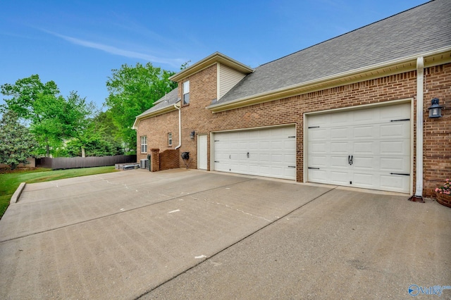 view of home's exterior with concrete driveway, roof with shingles, fence, brick siding, and a garage