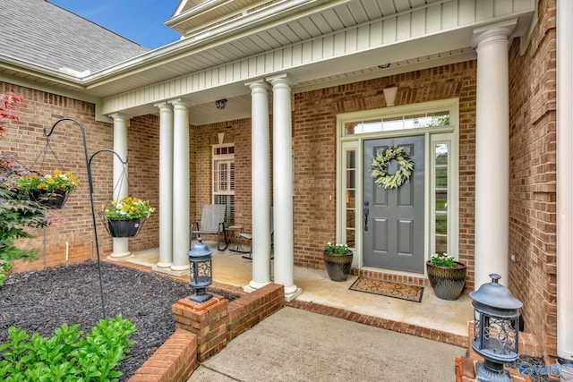 entrance to property with a porch, a shingled roof, and brick siding