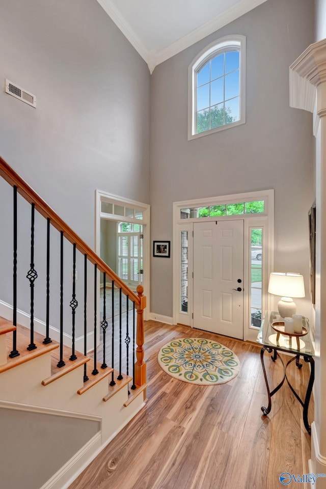 foyer featuring wood finished floors, visible vents, a healthy amount of sunlight, and crown molding