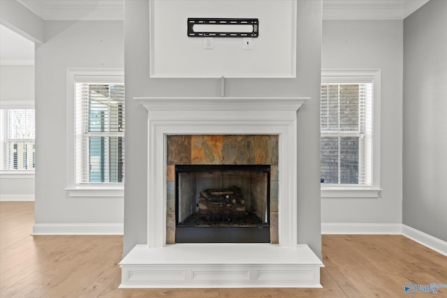 interior details featuring a fireplace with raised hearth, baseboards, wood finished floors, and crown molding