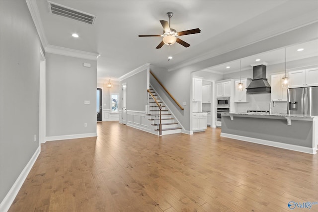 unfurnished living room with recessed lighting, visible vents, light wood-style floors, stairway, and crown molding