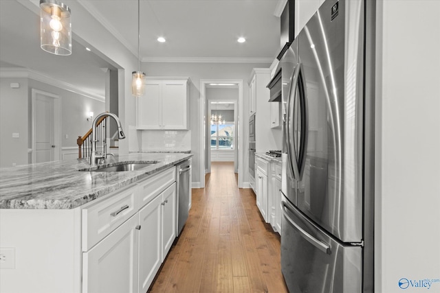 kitchen with a sink, white cabinetry, appliances with stainless steel finishes, hardwood / wood-style floors, and crown molding