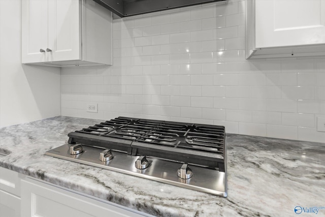 room details with light stone countertops, range hood, stainless steel gas stovetop, white cabinetry, and backsplash